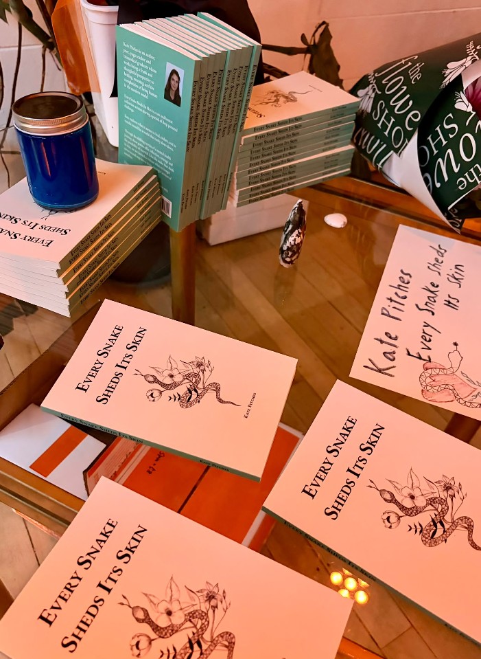 Copies of Every Snake Sheds Its Skin stacked and fanned on the book table, beside a hand-lettered sign.